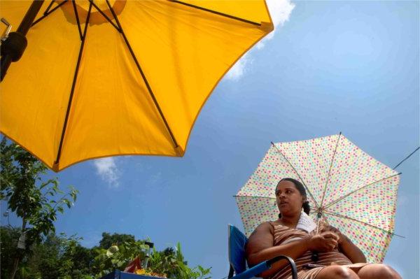  A person sits under an umbrella for shade while another yellow umbrella is nearby.