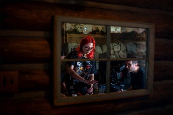  A person uses a movie camera on set of a film production while a person with bright red hair is seen reflected in a mirror. 