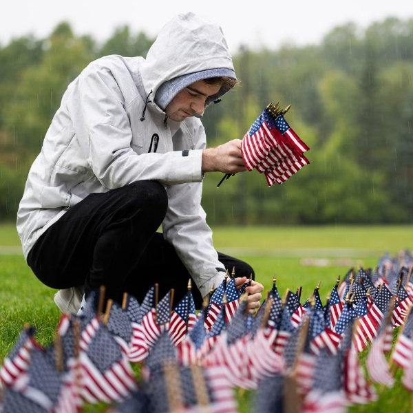 A person kneels while placing small American flags in the ground.