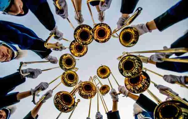 Marching band trombone players hold their instruments over their heads during a hype cheer.  