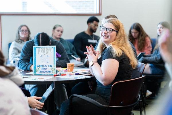 A smiling college student participates in a discussion.  