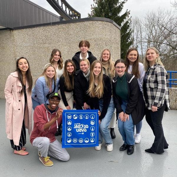 group of students, standing in two rows, holding a Global GVSU bandana; one person kneeling in front