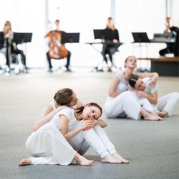 Dancers wearing white perform in front of musicians in the background.